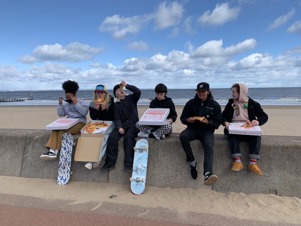 Group of kids sitting on promenade wall at Portobello eating pizza