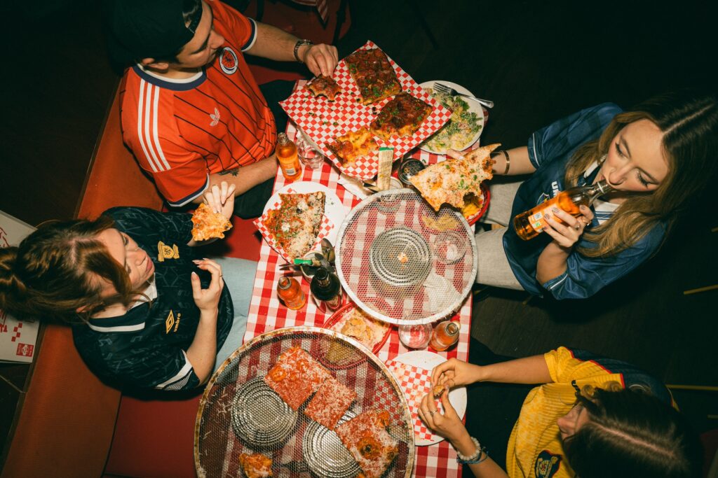 group of people in old school t shirts eating pizza for 2026 World Cup