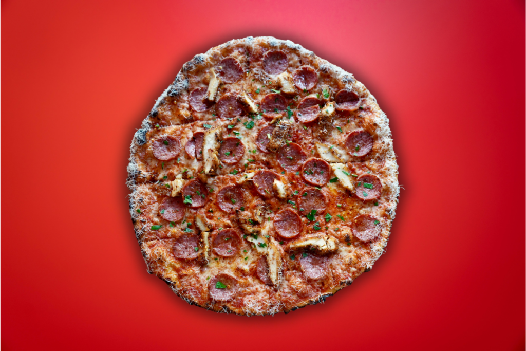 strips of chicken schnitzel, pepperoni and hot honey on New Haven style pizza with red background