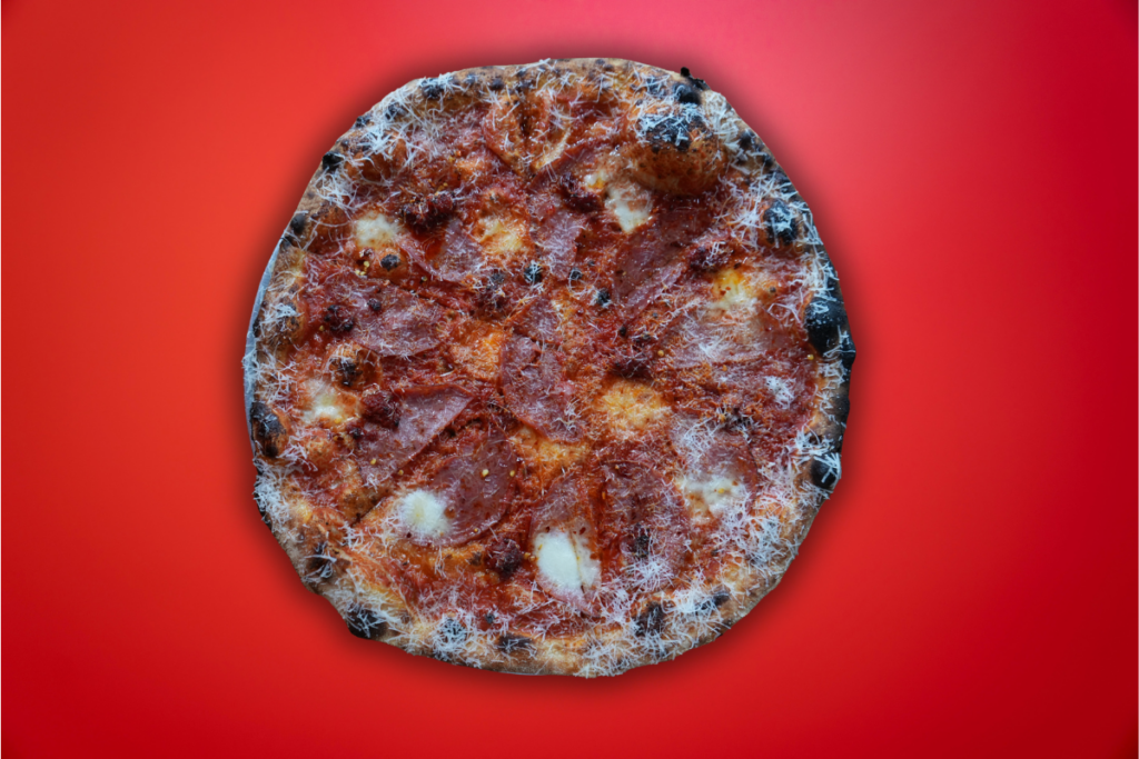 Salami milano, nduja, pecorino & hot heather honey on New York style pizza with red background
